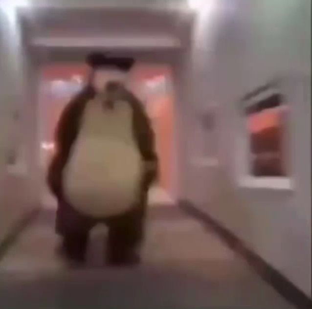 a teddy bear is walking down a hallway in a building .