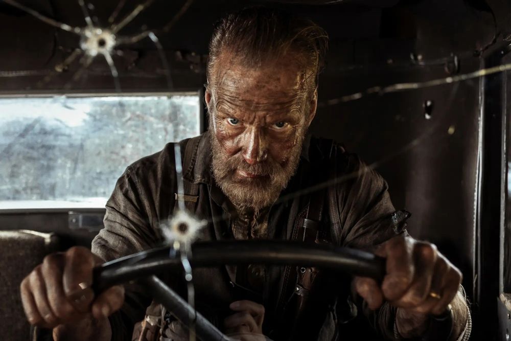 A man, bent on revenge, drives a vehicle with bullet holes in the windshield.