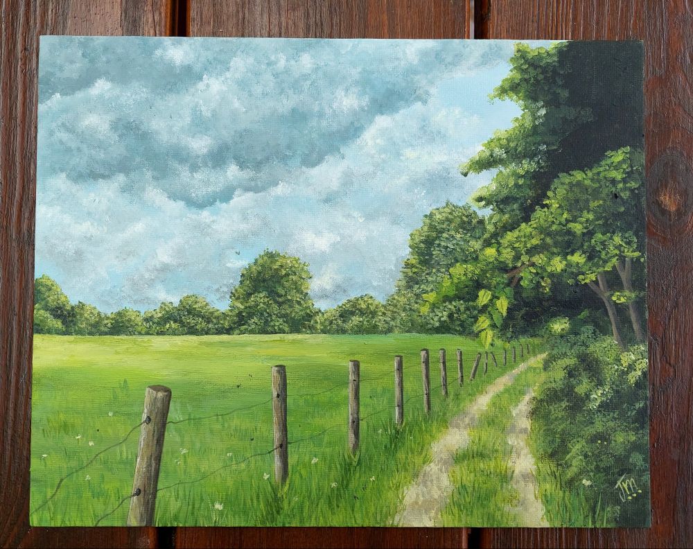 Photo d'une peinture sur toile plate. La peinture représente un paysage champêtre, avec un chemin à droite, un champ à gauche, une clôture en bois entre les deux et des arbres dans le fond.