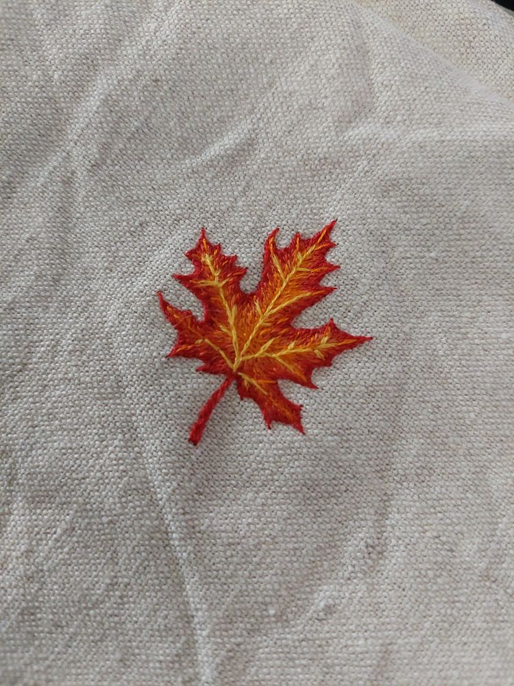 Photo d'une broderie de feuille d'érable dans les couleurs rouges orangers.