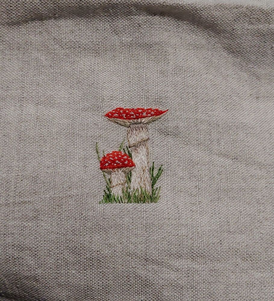 Photo qui montre une broderie de deux amanite tue-mouche sur un tissu écru.