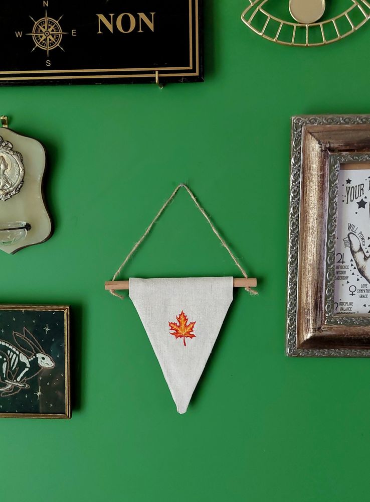 Photo d'un pan de mur vert avec des décorations accrochées dessus. Le centre de la photo est un fanion triangulaire brodé.