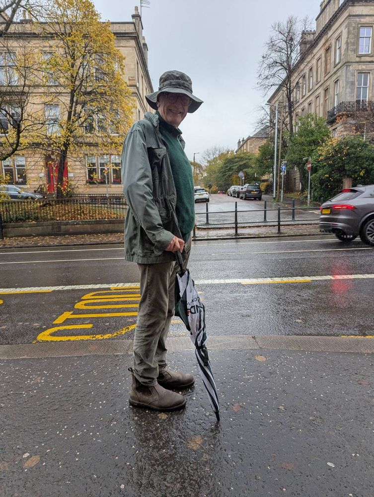 Tom with his rain hat and umbrella preparing to flag down the bus. 