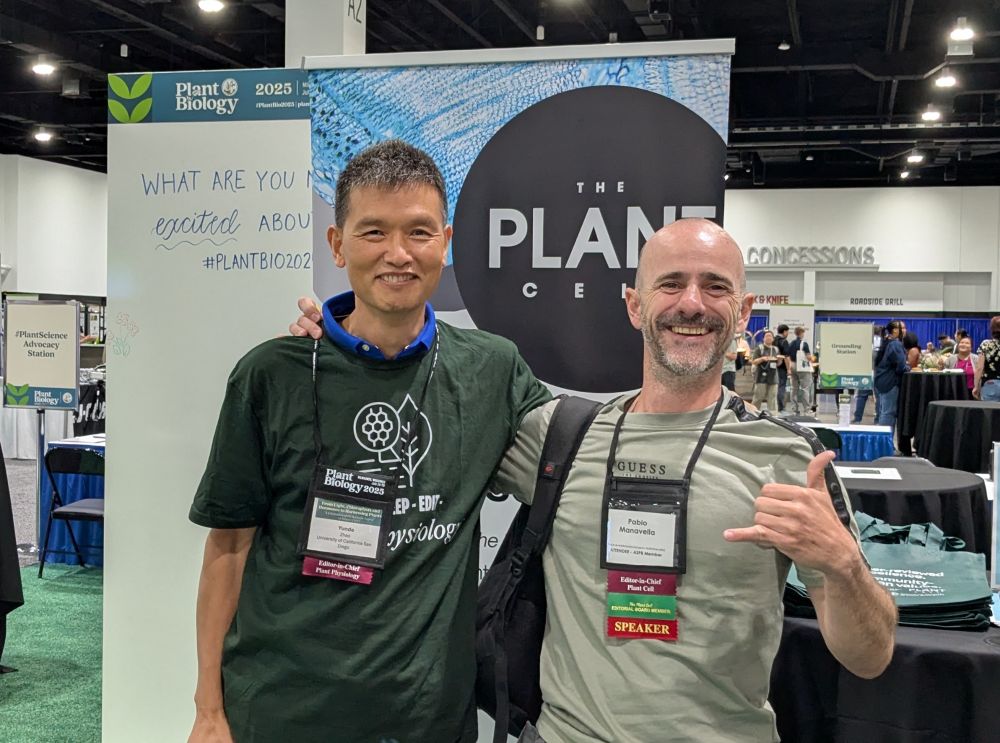 Yunde and Pablo smiling in front of a Plant Cell poster. 