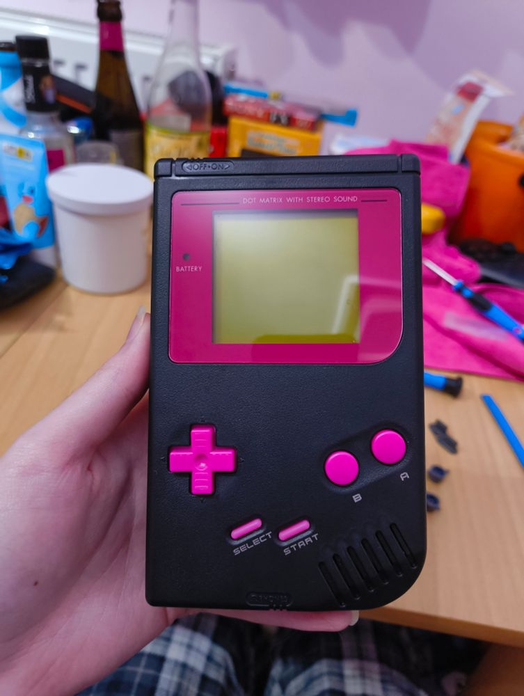 a black dmg gameboy with a pink screen lens and buttons 