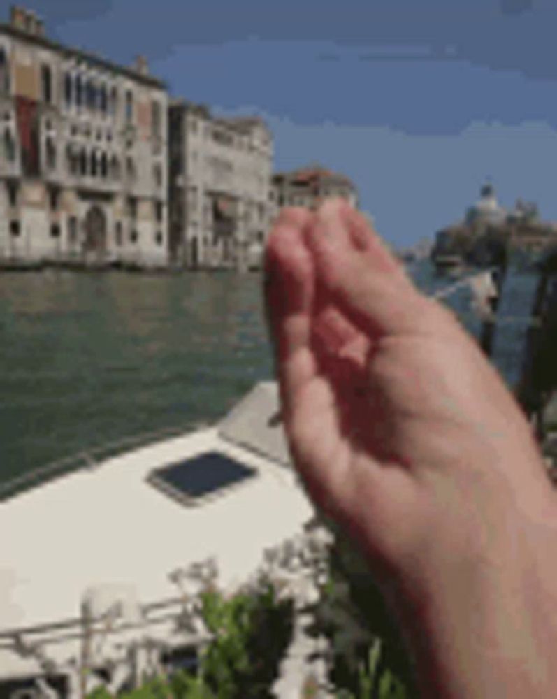 a person 's hand is reaching out towards a boat in the water