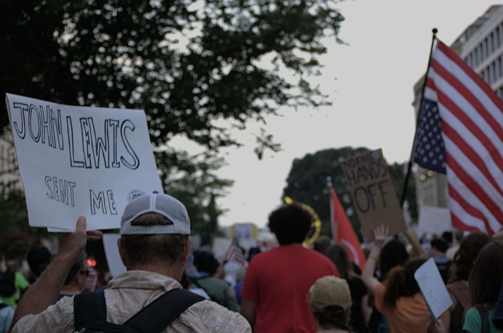 Many peaceful protesters march toward the mall. A man holds a sign reading "John Lewis Sent Me"
