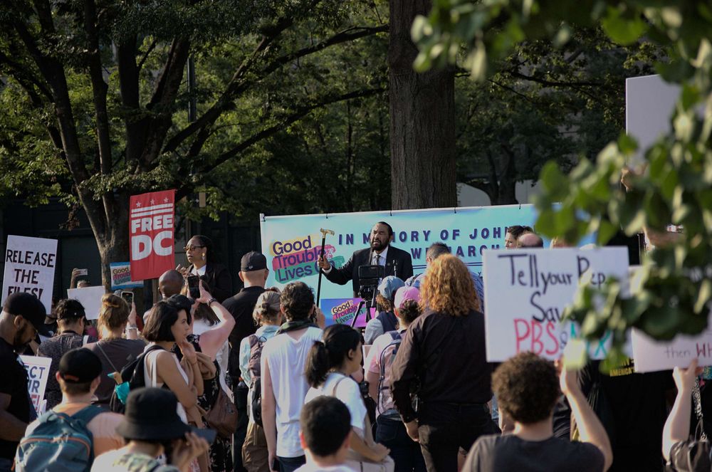 Democratic Representative from Texas, Al Green, addressing the peaceful protesters from a stage. He speaks energetically about John Lewis and holds his cane aloft.