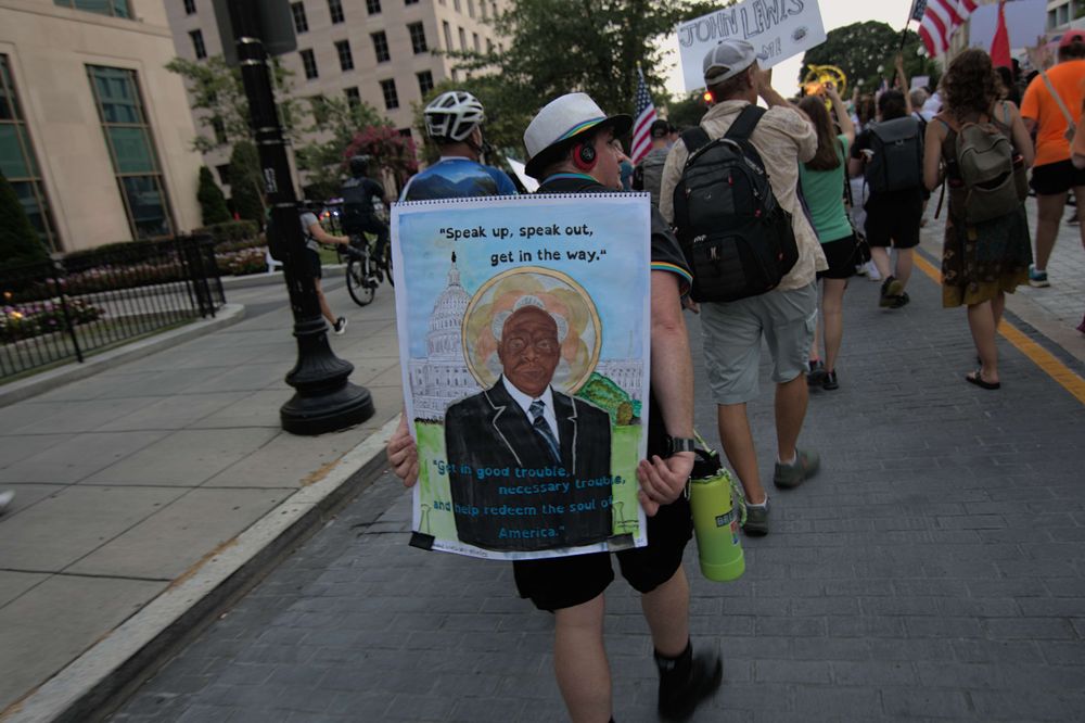 Peaceful protesters continue their march toward the mall. One man holds behind him a full color painted portrait of John Lewis with quotes "Speak up, speak out, get in the way" and "Get in good trouble, necessary trouble, and help redeem the soul of America"
