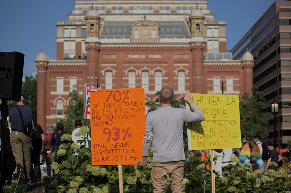 A gentleman stands with two signs, one reads "70% of those taken by the ICE Gestapo have no criminal record, 93% have never committed a serious crime" the other "Chinga La Migra; Fascist thugs are kidnapping our neighbors with NO due process!"