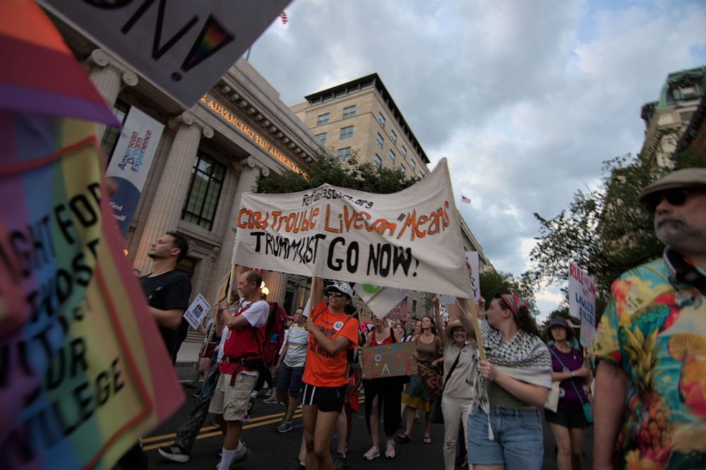 Many peaceful protesters continue marching. Three hold a large banner that reads "Good Trouble Lives On Means trump Must Go Now!" with their organization website above (sorry, I can't make it out)