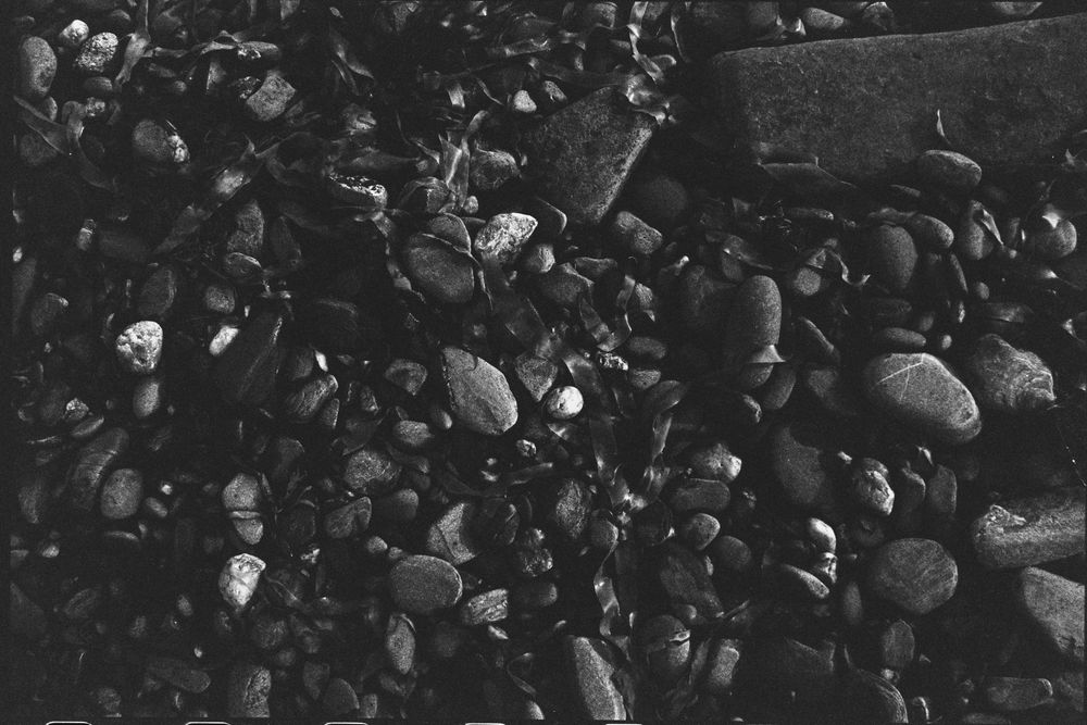 A dark and underexposed black & white film photo of rocks on a beach, only rocks are visible and they show a range of light and texture 