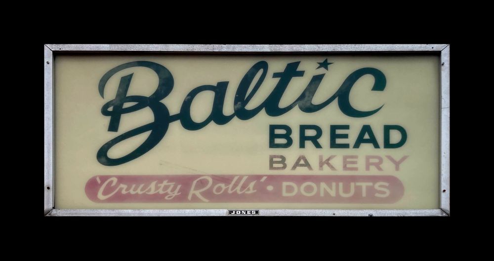 A hand-lettered sign that says “Baltic Bread Bakery” and then underneath, ‘Crusty Rolls’ • Donuts