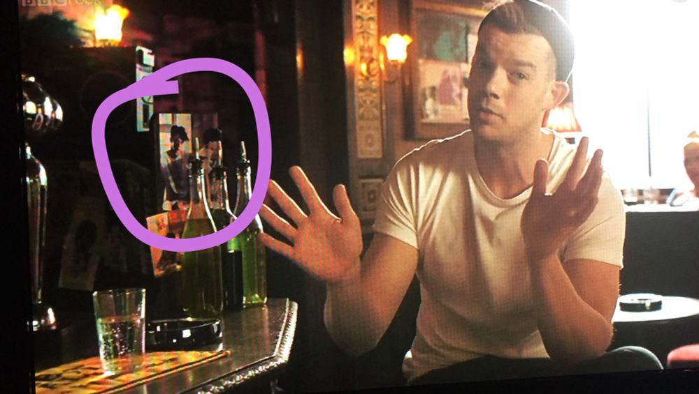 Russell Tovey sits at a bar. I’ve circled my photo on the wall behind him. 