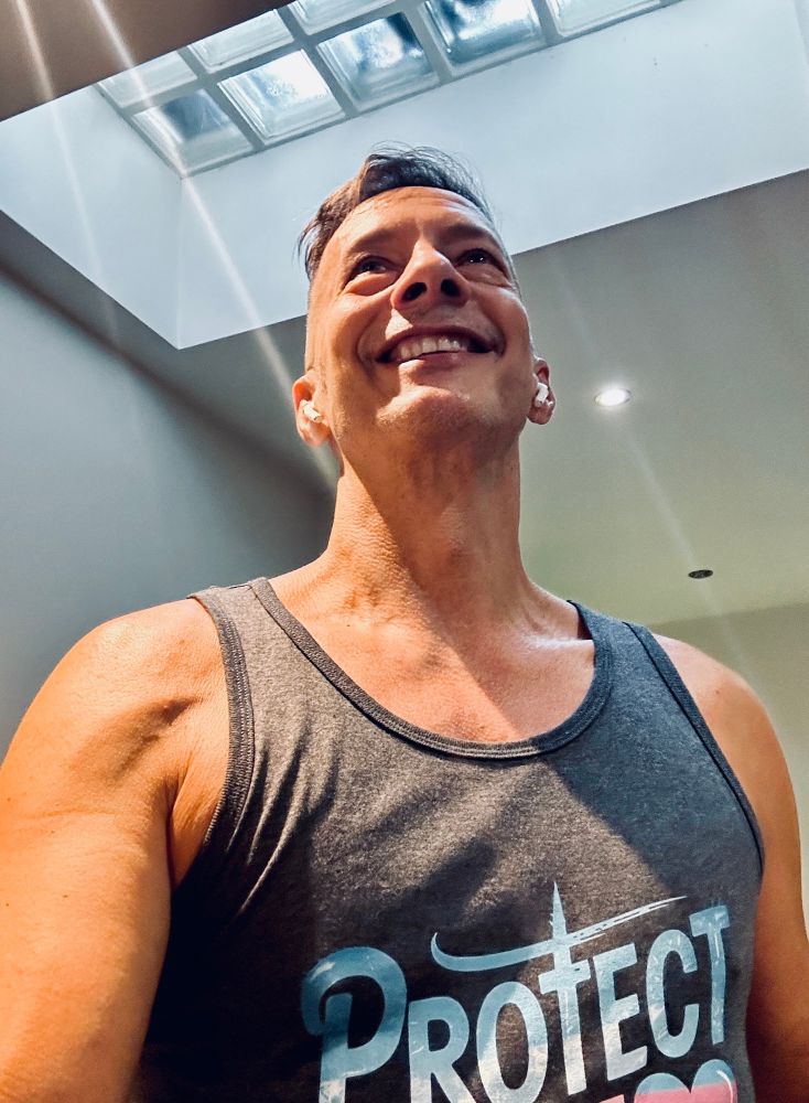 Me last week, working out at home. I’m wearing a smile and a Protect the Dolls vest. My hair is short, grey and awesome. 