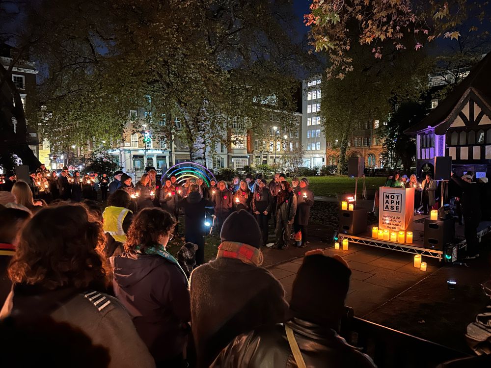 It is dark. A candlelit chorus are singing John Lennon’s Imagine. A crowd hold more candles. 