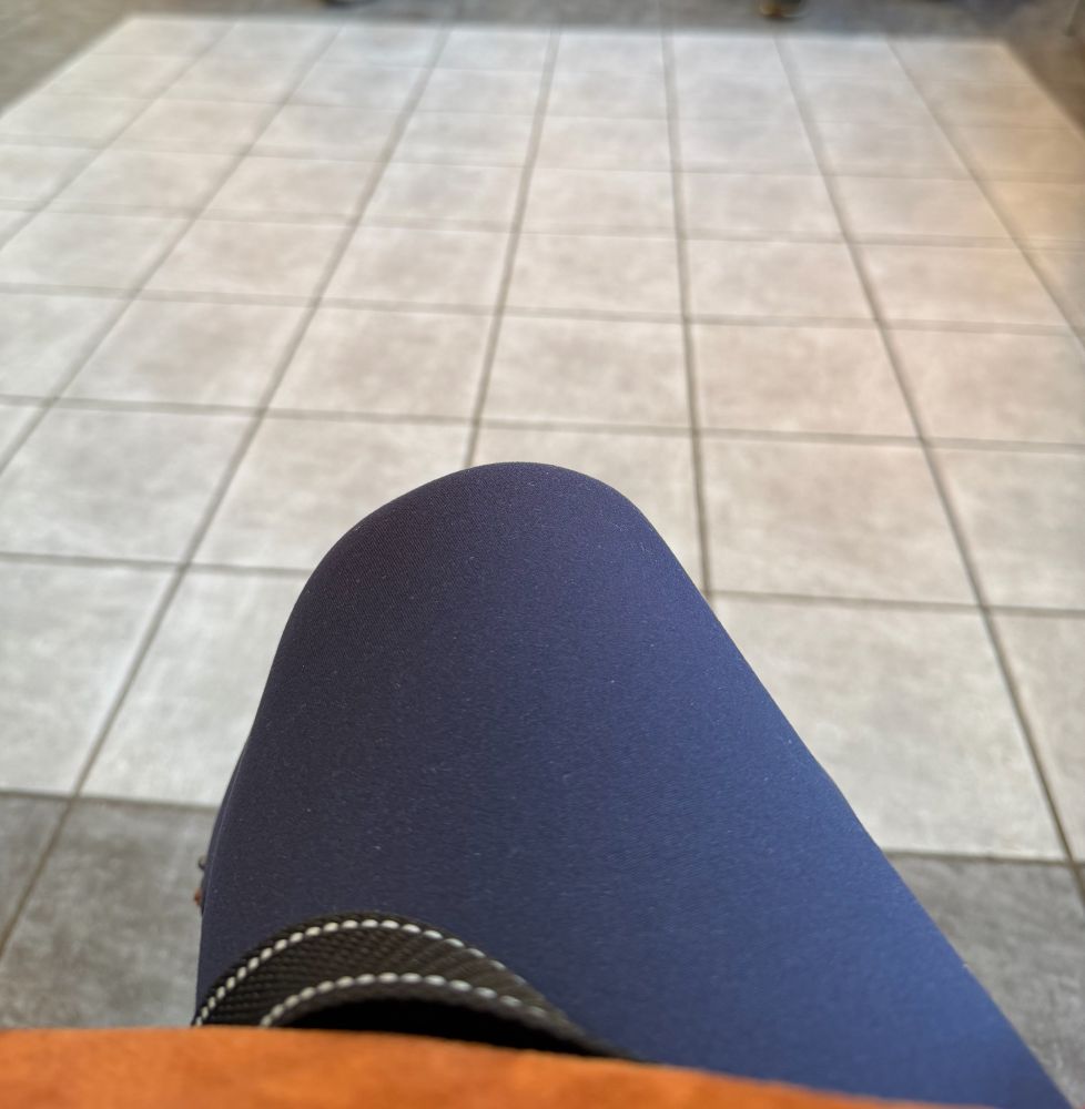 Ein hell gefliester Boden, im Vordergrund ein Knie in einer blauen Hose