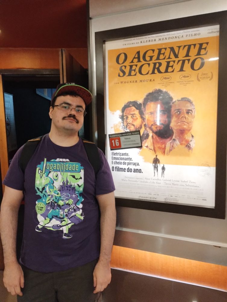 Eu na frente do cartaz de O Agente Secreto na entrada da sala de cinema 