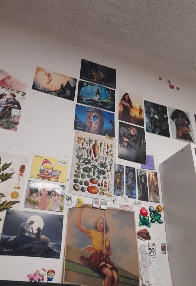 A white wall with posters and art covering it. There are some empty spaces with bluetack markings where paper has been taken down.