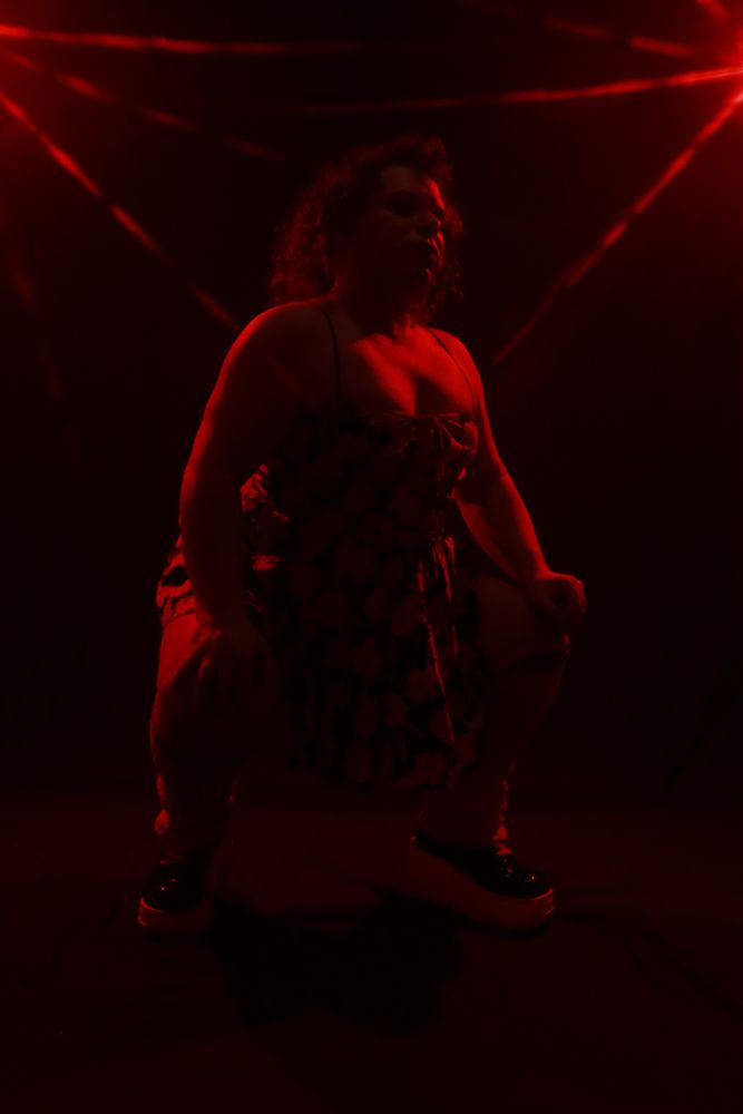 Nikki Lev crouched, head cocked, in red light. 