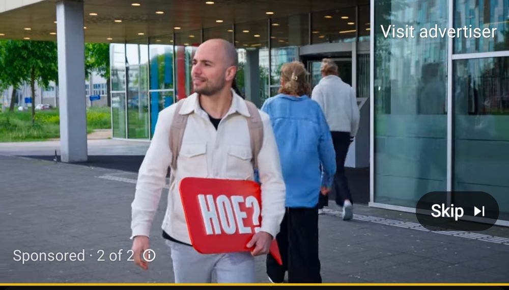 YouTube ad with a Dutch man in the foreground outside of an office building with glass paneling and trees in the background, women facing away in sweaters in the midground. The man is holding a red sign that says, "hoe?" while smiling and looking perpendicularly to the left from the vantage point 