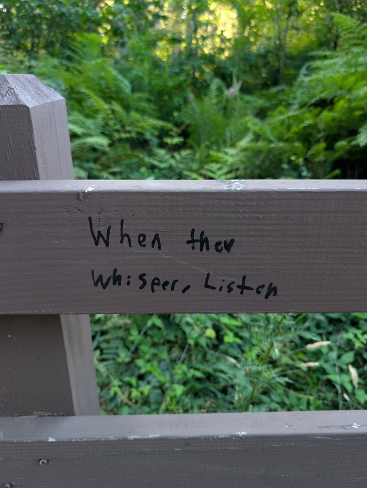 A handwritten message on a fence that says "When they whisper, listen"
