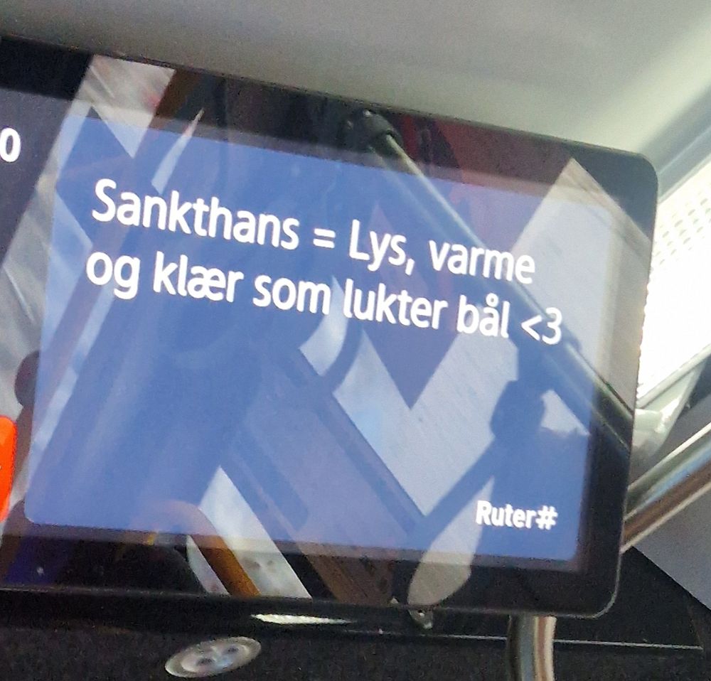 Informasjonsskjerm for kollektivselskapet Ruter på en bybuss i Oslo. Skjermen viser teksten "Sankthans = Lys, varme og klær som lukter bål <3"