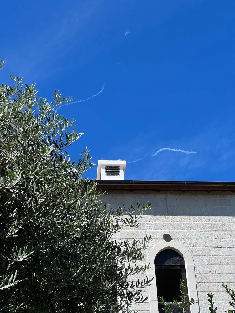 Im Vordergrund ein Baum und ein Häuserdach, am Himmel sieht man zwei Spuren von Raketen.