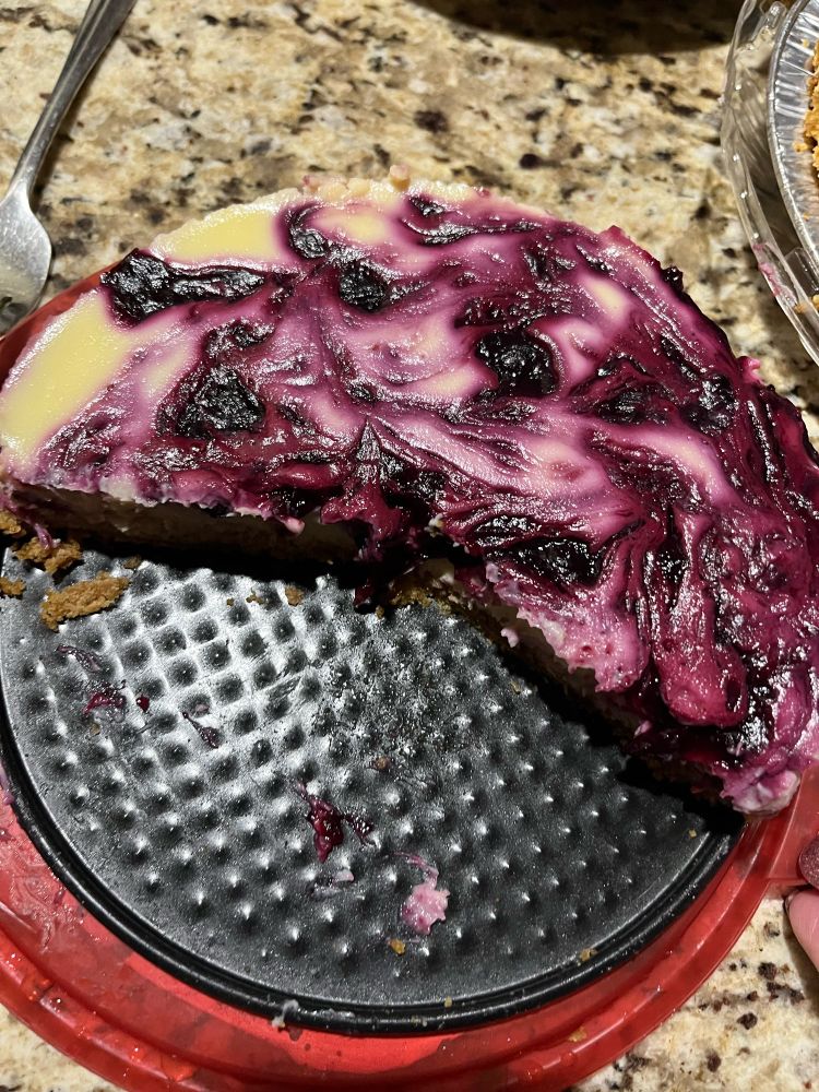 Half-consumed blueberry swirl cheesecake on a black springform pan base