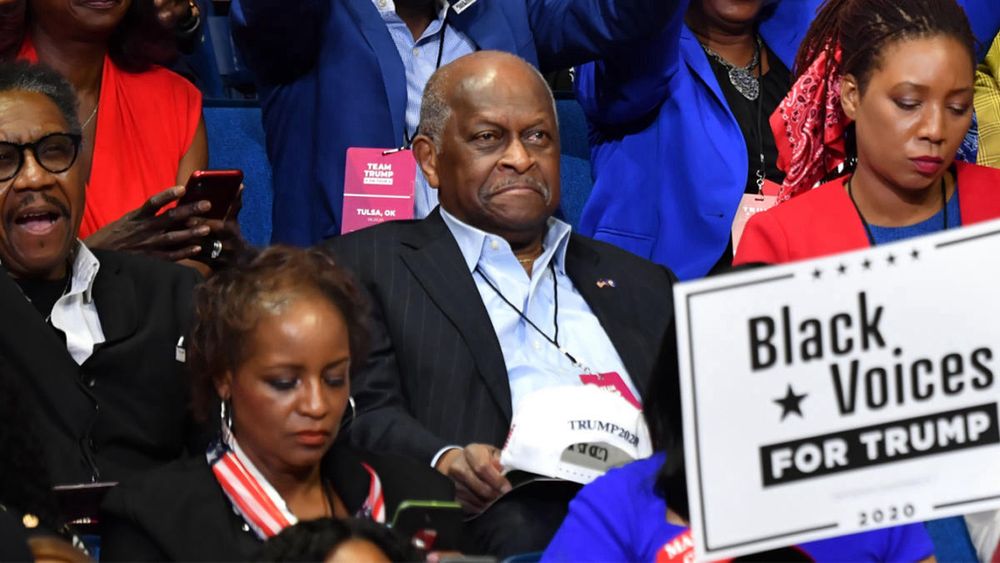 Herman Cain sitting in the crowd without a mask or any attempt social distancing.
