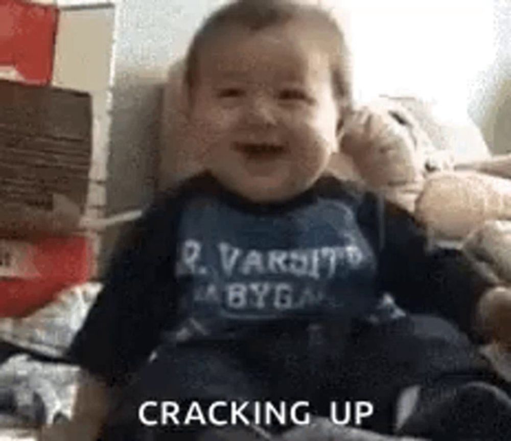 a baby is sitting on a bed and smiling while wearing a varsity shirt .