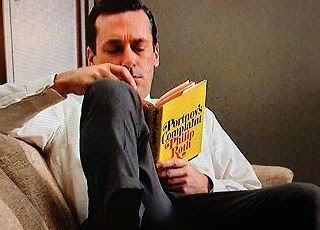 Don Draper, a dapper man in a white shirt and tie, reading Portnoy's Complaint