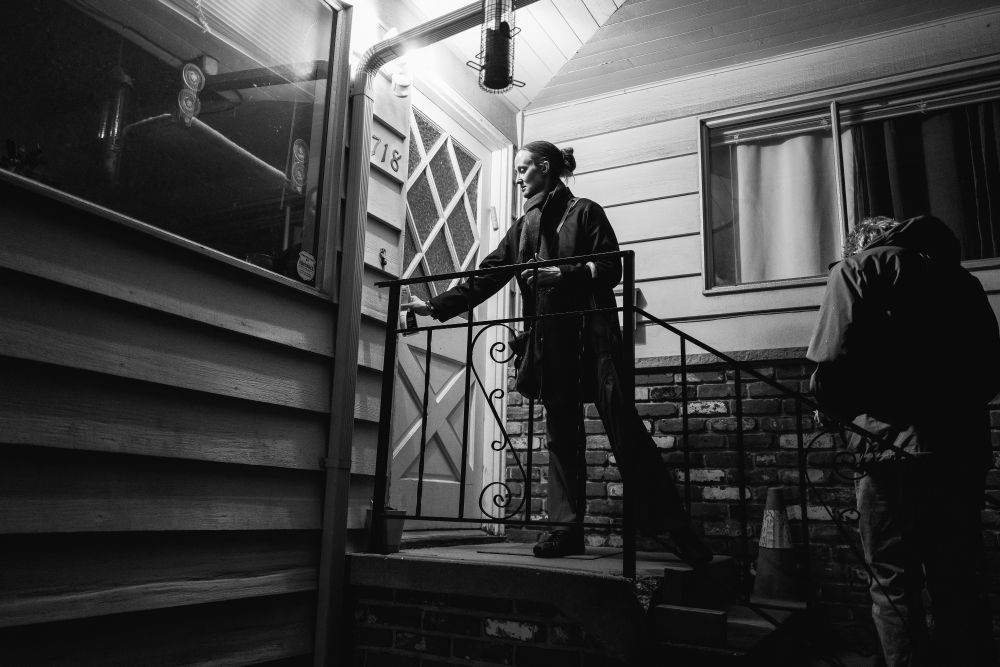 A black and white photo of Katie Wilson knocking on a door of a single family home while door knocking for her campaign