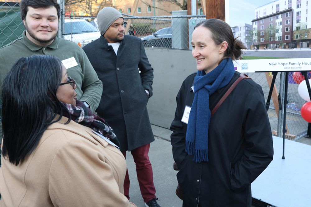 A photo of Katie Wilson with her hands in her pockets, smiling at three community members attending the groundbreaking ceremony