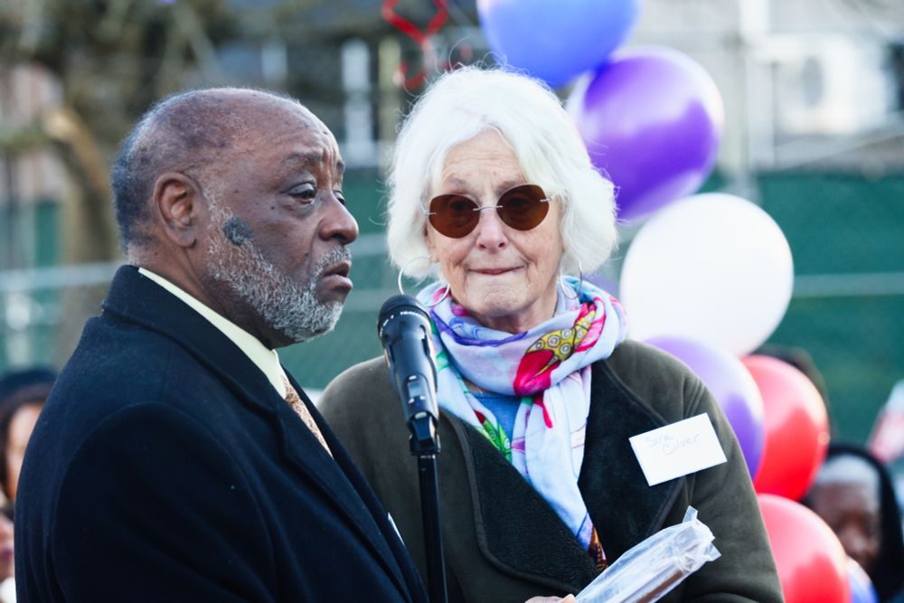 A photo of Rev. Dr. Robert L. Jeffrey, Sr. into a microphone at the groundbreaking ceremony with a woman with white hair and glasses by his side