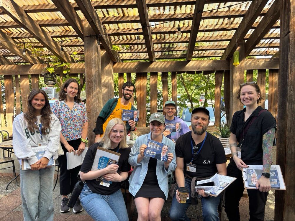 A group of 8 people hold clipboards and campaign literature before a doorknocking session.
