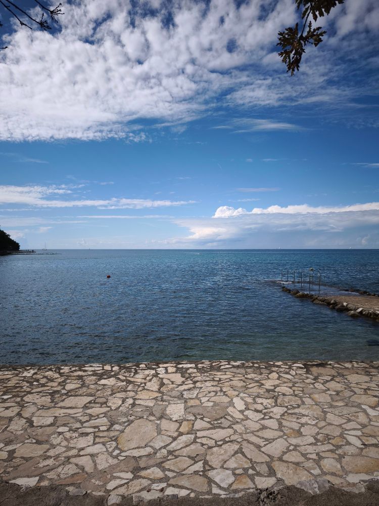 Blick auf den leeren kroatischen Stein Strand, ruhiges, klares Meer, ganz leicht bewölkter blauer Himnel