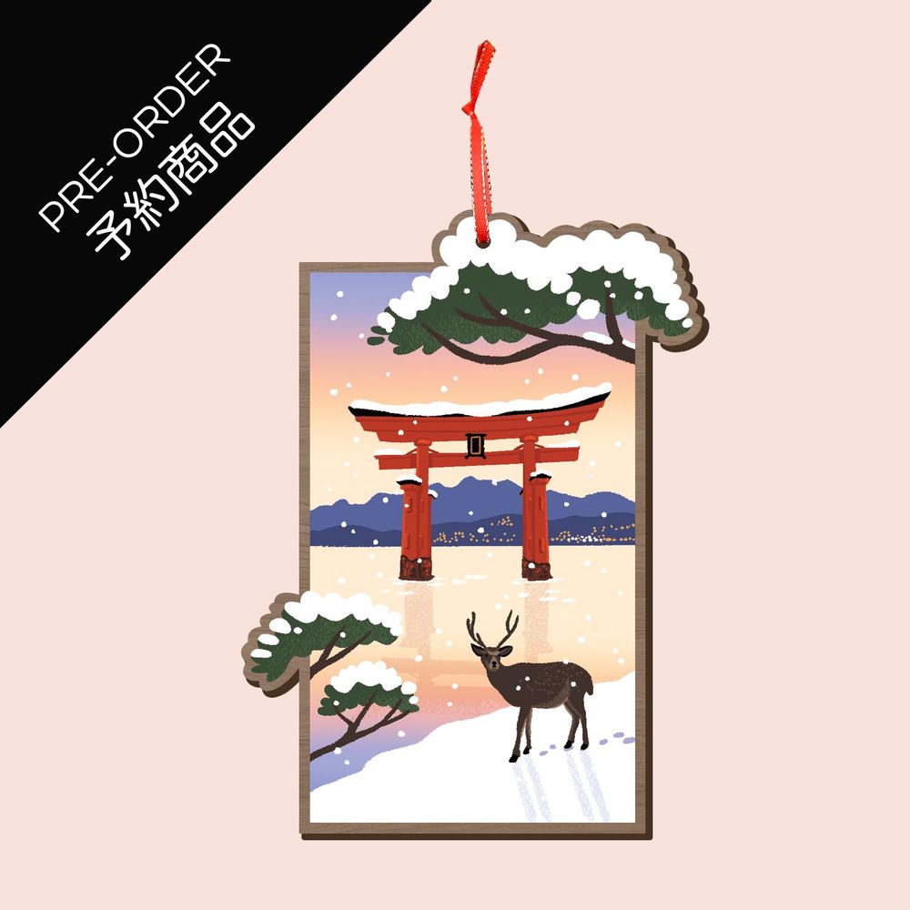 A mocked up image depicting a wooden Christmas tree ornament. The ornament features an illustration of a sunset on the island of Miyajima, Japan, with fresh snow piled up on the red torii gate floating in the sea, as well as on the pine trees framing the scene. A lone shika deer is looking on in the foreground.