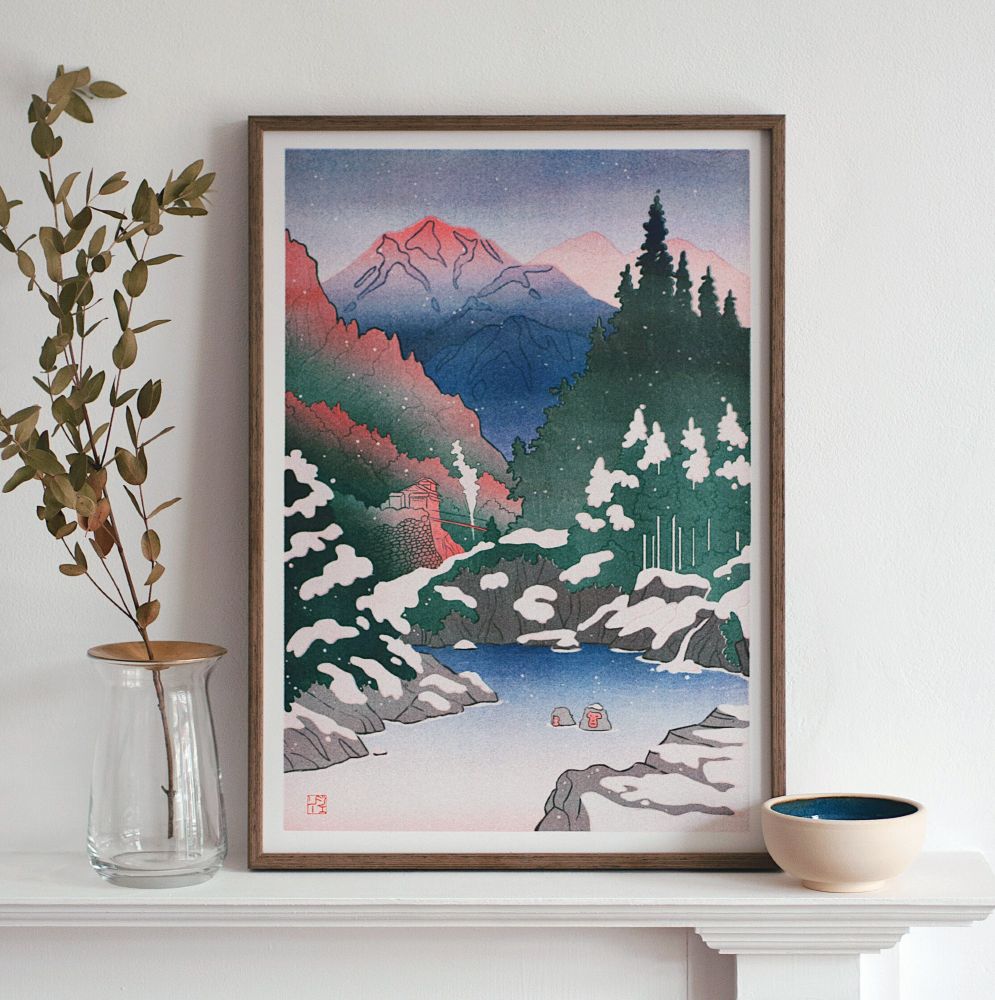 A framed print of a snowy Japanese mountain scene reminiscent of a woodblock print, with snow monkeys bathing in the foreground.