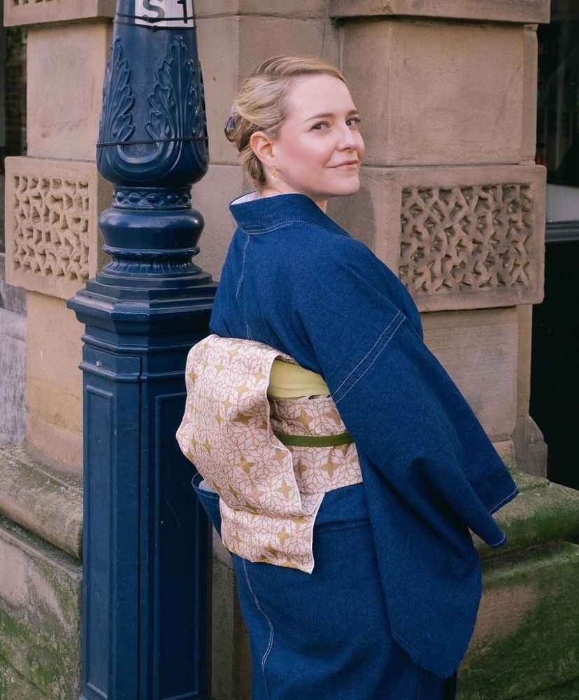 A blonde woman (me!) wearing a denim kimono with a light brown and beige obi belt. The background is a British street corner with a blue iron lamppost.
