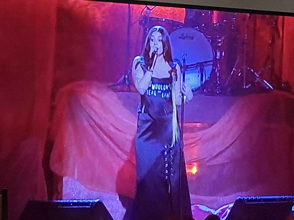 Thelma Plum with long black straight hair wearing a dress with the words "You Wouldn't Steal Our Land" in the font of the you wouldn't steal a car anti-piracy ad