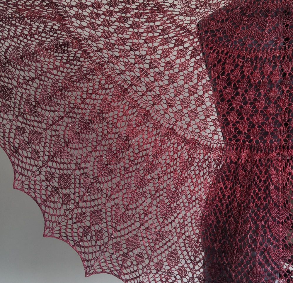 A red lace shawl held up to the light so that you can see the pattern