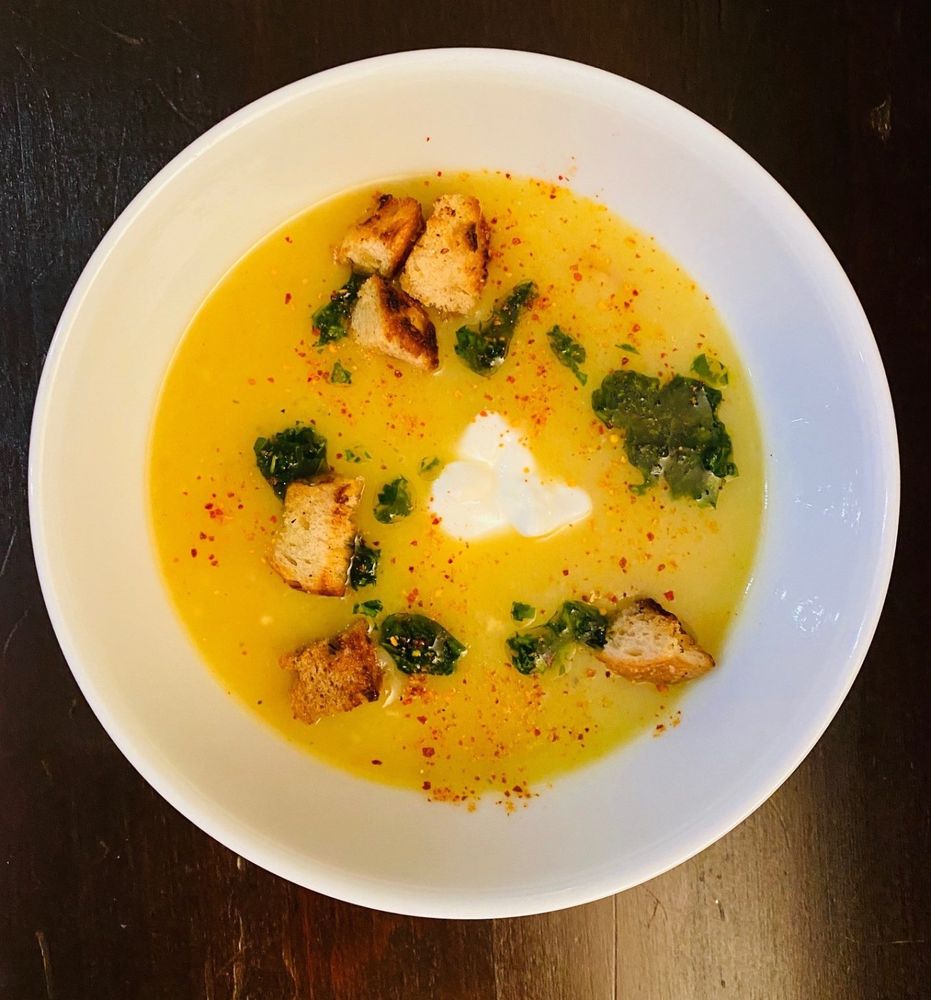 Kartoffelsuppe mit Croûtons, Kräuteröl und einem Klecks Joghurt in weißer Schale.