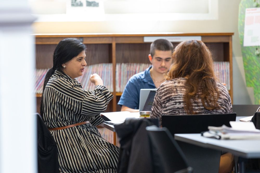 Three people sit around a table in a library.