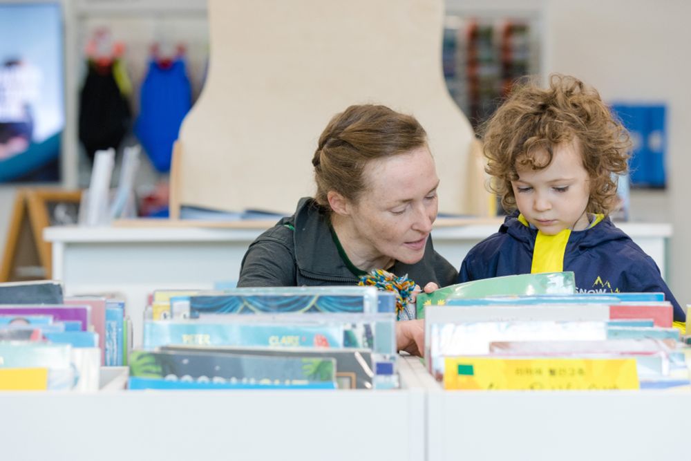 A woman helps a child with a book in a library.
