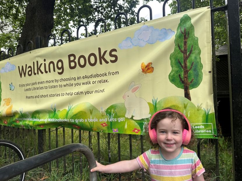 A young girl stands in front of a banner for Leeds Libraries' 'Walking Books' initiative.
