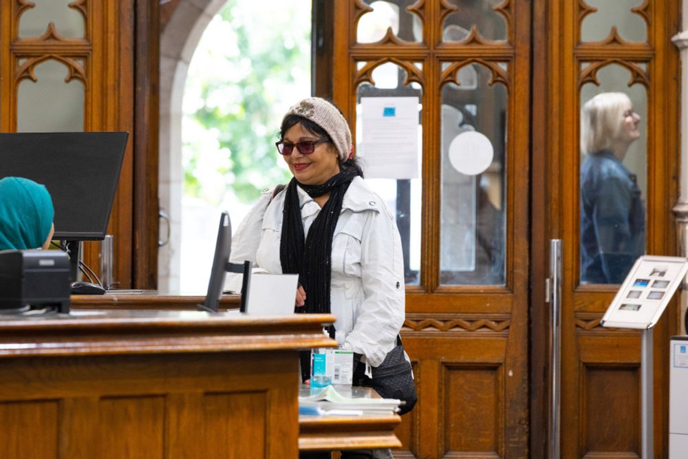 A woman speaks to a female librarian in a wood panelled library.