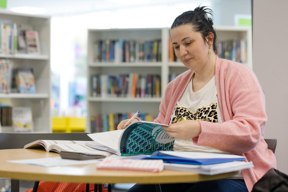 A woman smiles as she writes in a notepad in a library.