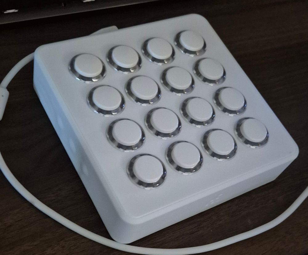 A MIDI Fighter Spectra. It is a white box covered in 16 white arcade game buttons. They light up with custom colours when pressed