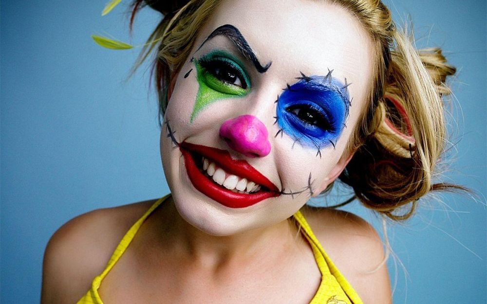 A cute blonde girl wearing a yellow bikini and clown face paint.